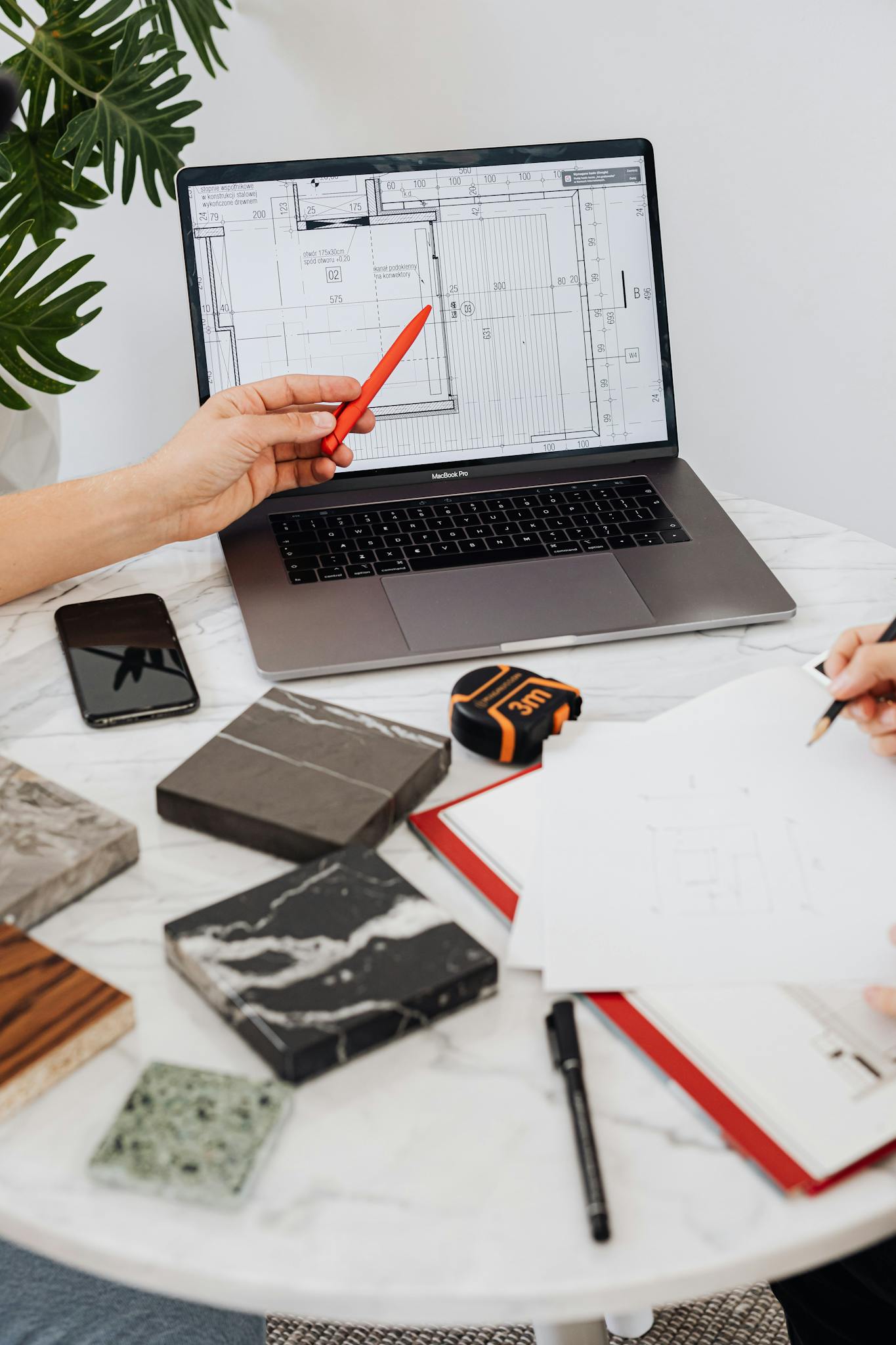 Interior designers reviewing tile samples and floor plans using a laptop and pen on a marble table.